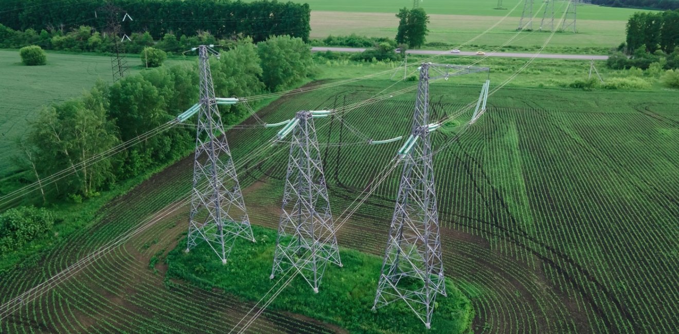 High voltage electric power tower in a green agricultural landscape at beautiful sunset