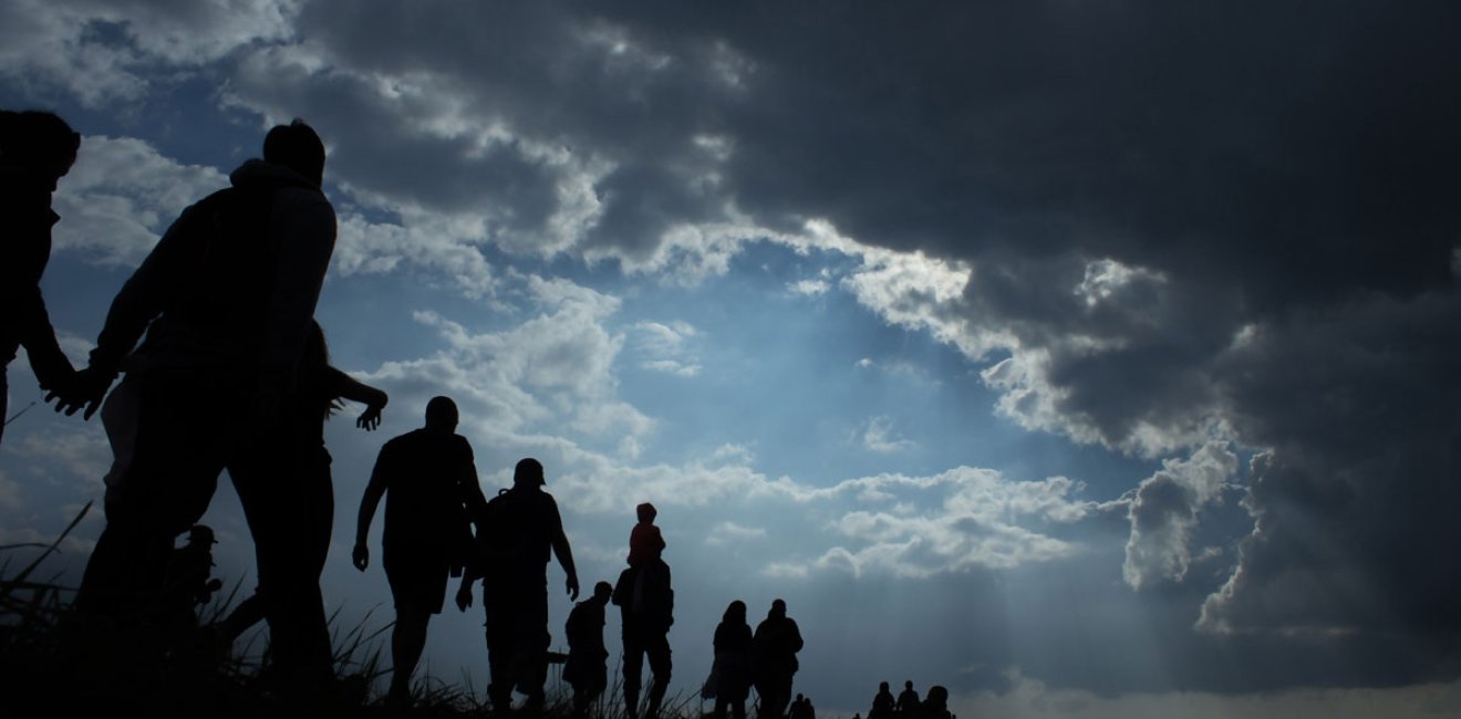 Sun rays illuminate people. Immigration of people. Blue sky with dark clouds