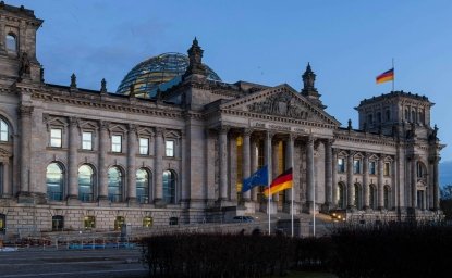 The Bundestag building at dusk, with German and EU flags waving in front. 