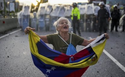 Consuelo Marquez holds a Venezuelan flag in front of police blocking demonstrations against the official election results declaring President Nicolas Maduro's reelection, the day after the vote in Caracas, Venezuela, Monday, July 29, 2024. 