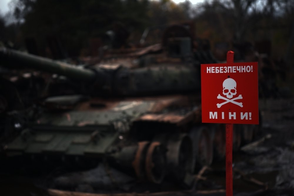 A sign reading 'DANGER MINES' with a destroyed tank in the background
