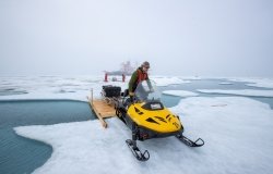 Matthew Shupe drives a snowmobile over a bridge toward a measurement site on Jul 29, 2020, photo courtesy of Alfred-Wegener-Institut/Lianna Nixon (CC-BY 4.0). 