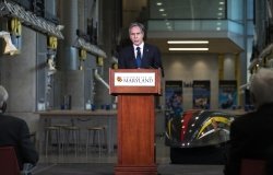 Secretary of State Antony Blinken stands at a podium with a University of Maryland logo on the front, delivering a speech.