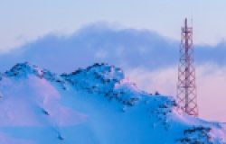 Telecommunication tower on the slope of a snowy mountain. Winter arctic landscape. View of the mountain top and the metal tower with antennas. Communication in the far north in the polar region.