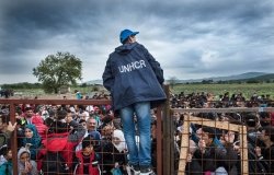 Gevjelija, Macedonia - September 26, 2015. A UNHCR employee talks to refugees as they wait during a rainstorm to enter inside a refugee camp near the town of Gevgelija at the Macedonian - Greek border