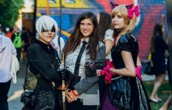 Three women dressed in fantasy and punk costumes standing in front of a mural at a festival in Kyiv