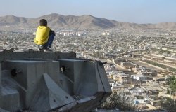 A boy sits on a ledge overlooking Kabul