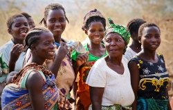 A group of colorfully dressed African women and babies gather at a clean water pump